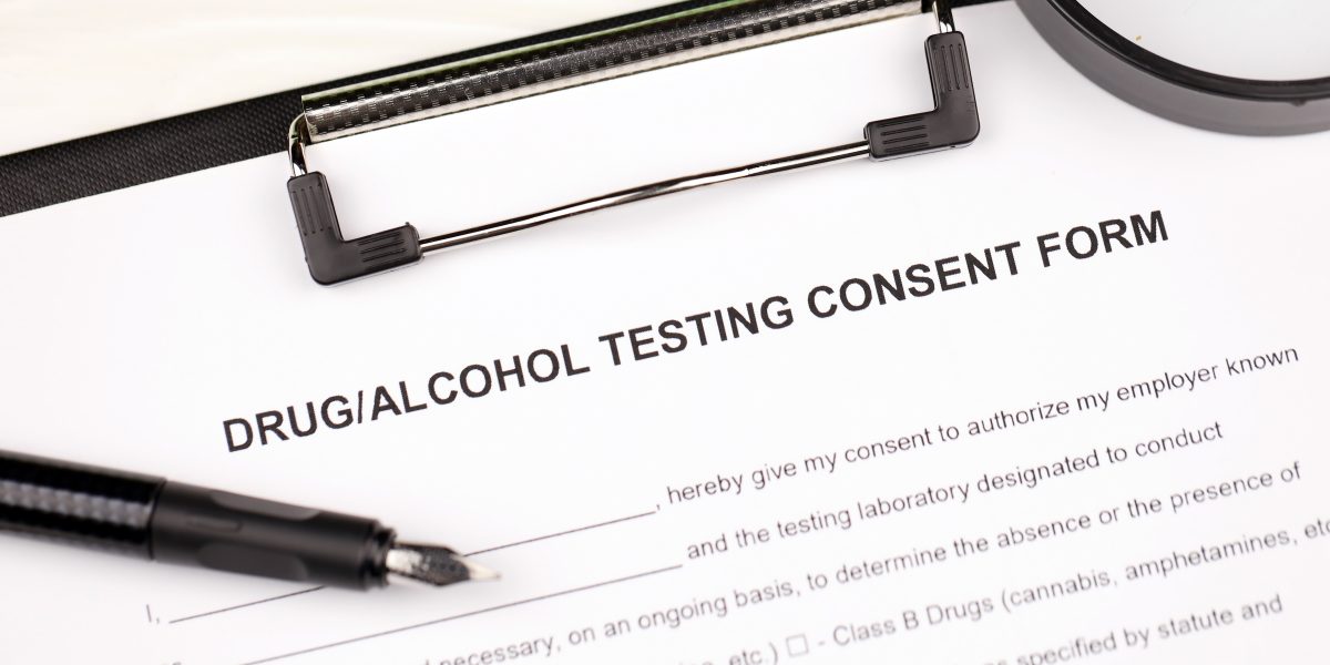 Drug and alcohol testing consent form on A4 tablet lies on office table with pen and magnifying glass close up