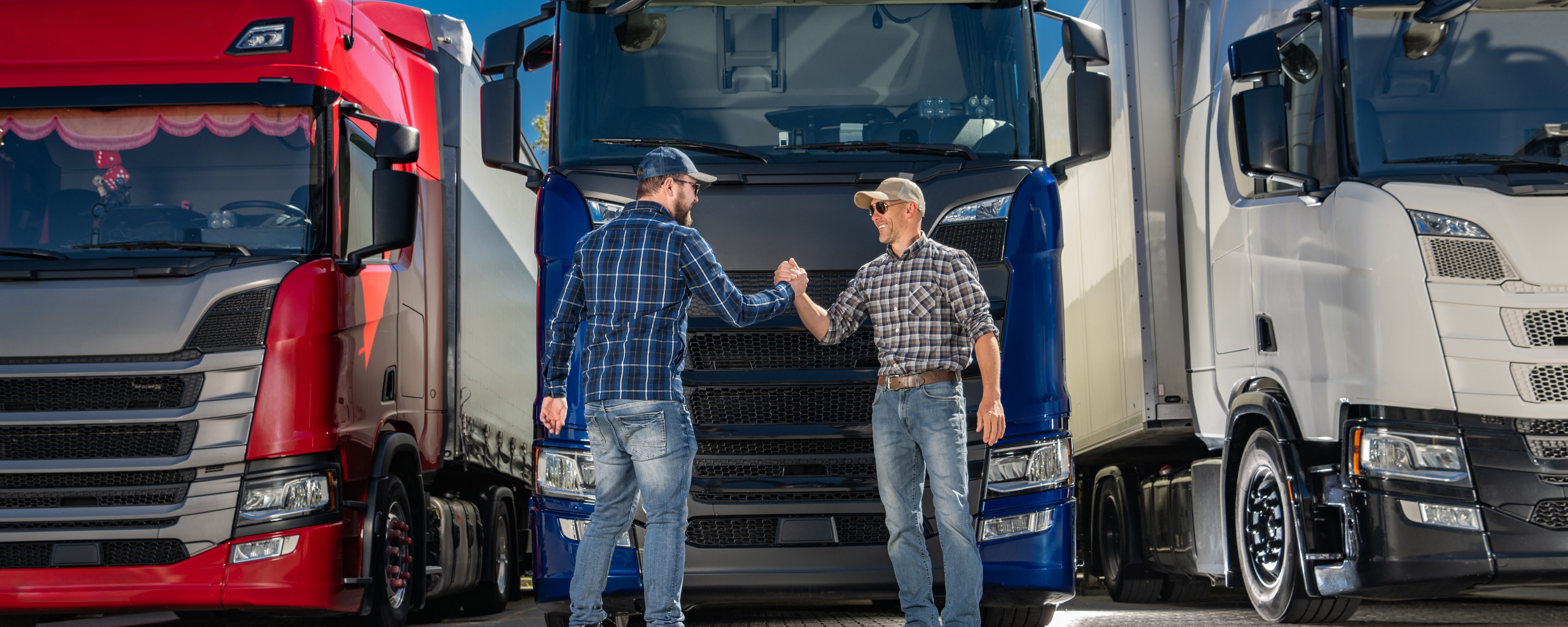 Two caucasian semi truck drivers shaking hands in front of a group of euro trucks.